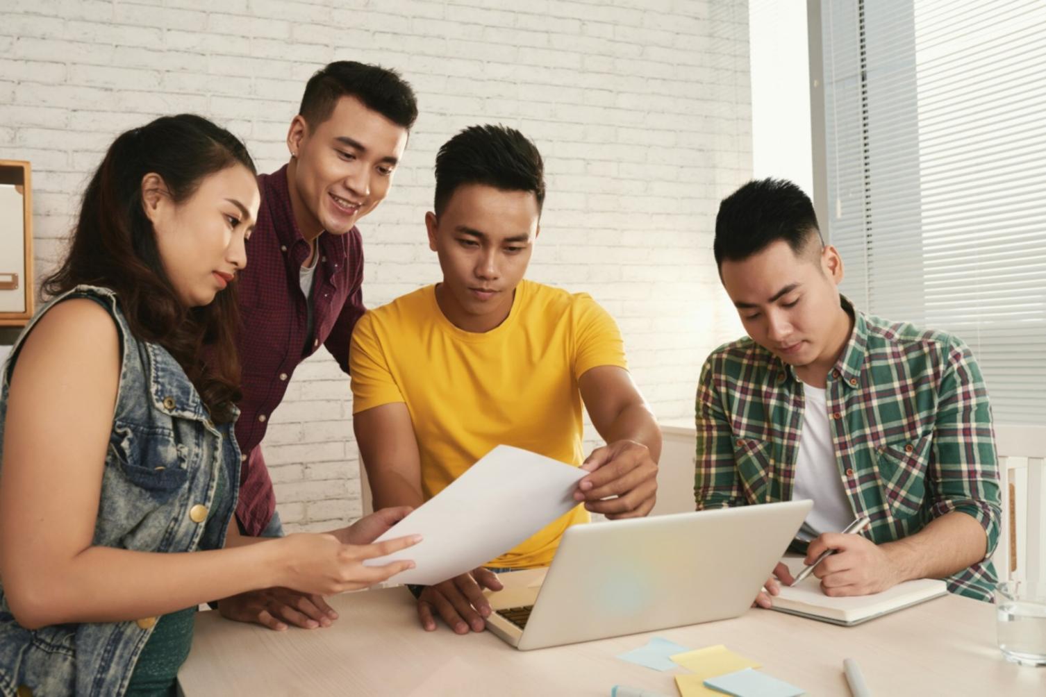 Student working on laptop with research materials and notes spread across desk